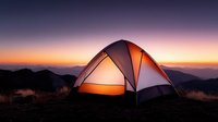 Illuminated camping tent glowing warmly against dramatic sunset sky in mountain wilderness. Adventure travel and outdoor recreation concept for hiking enthusiasts.