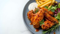Grilled chicken wings with golden french fries and fresh herbs on dark plate. Restaurant meal with crispy potatoes and barbecue sauce for dining menu.