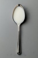 Silver spoon filled with fresh white milk or cream on neutral background for culinary and dairy product photography.