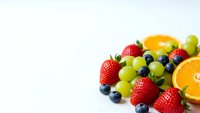 Fresh mixed fruits including strawberries, blueberries, green grapes and orange slices arranged on white background for healthy eating concepts.