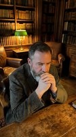 Thoughtful mature Caucasian businessman in tweed jacket contemplating in classic library with vintage books and warm lighting for professional content.