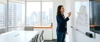 Professional businesswoman presenting strategy on whiteboard in modern corporate office with city skyline view during team meeting.
