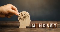 Hand holding wooden head silhouette with gear mechanisms representing mindset and mental processes for business growth and personal development.