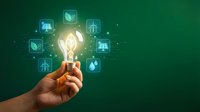 Hand holding glowing light bulb with green energy icons on emerald background representing sustainable innovation and eco-friendly technology solutions.