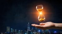 Glowing hourglass floating above open palm against dark blue background with city lights, symbolizing time management and business deadline concepts.
