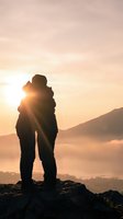 Silhouette of loving couple embracing on mountain peak during golden sunset with warm sky and scenic landscape background for romantic concepts.