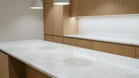 Modern minimalist kitchen with white marble countertops and warm wood cabinetry featuring clean lines and contemporary pendant lighting for interior design.