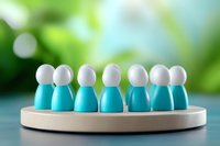 Small white and turquoise wooden figures standing in circle on round platform against blurred green background, representing team unity and collaboration concept.