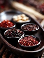 Assorted dried chili peppers and spices in black ceramic bowls on wooden tray, macro food photography with selective focus for culinary and cooking concepts.