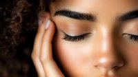 Young mixed-race woman with closed eyes and natural makeup touching face in peaceful skincare routine moment with soft lighting for beauty and wellness concepts.