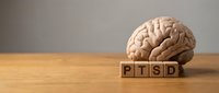Anatomical brain model with wooden blocks spelling PTSD on a wooden table, representing post-traumatic stress disorder awareness and mental health.