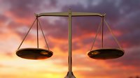 Golden scales of justice balanced against dramatic sunset sky with purple and orange clouds symbolizing legal fairness and judicial system.