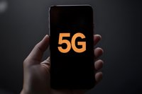 Hand holding smartphone displaying bright orange 5G text on black screen, representing next-generation mobile network technology.