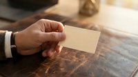 Professional businessman hand holding blank business card mockup on wooden desk surface for corporate branding and marketing materials design.