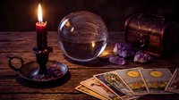 Mystical fortune telling setup with crystal ball, tarot cards, candle and amethyst crystals on wooden table for divination and spiritual guidance sessions.