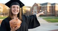 Young Caucasian female graduate in cap and gown holding education fund piggy bank on campus, celebrating academic achievement and financial planning.