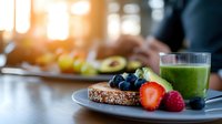 Healthy breakfast plate with whole grain bread, fresh berries and green smoothie on wooden table in morning sunlight, selective focus on foreground.