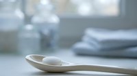 Wooden spoon with white pills on kitchen counter near window with natural light and folded towels in background for healthcare concept.