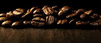 Roasted coffee beans scattered on dark textured surface with warm lighting creating rich brown tones and aromatic appeal for cafe and beverage concepts.