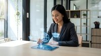 Professional Asian businesswoman using futuristic holographic tablet technology in modern office workspace for digital innovation and virtual reality applications.