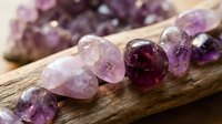 Collection of polished amethyst gemstones in various purple shades arranged on rustic wooden surface for jewelry making and crystal healing practices.