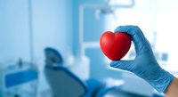 Hand in blue medical glove holding red heart in dental clinic, symbolizing care, health, and patient love in dentistry.