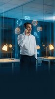 Young male professional wearing white shirt and headphones talking on phone in modern office with glowing communication icons floating around him, representing digital connectivity and business communication.