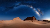 Majestic Milky Way galaxy arches over desert sand dunes and rocky formations at night, creating dramatic natural landscape under starry night sky.