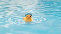 Yellow rubber duck floating in clear blue water with gentle ripples creating concentric circles around toy for bath time and childhood memories.