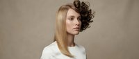 Young Caucasian woman with split hairstyle showing straight blonde and curly brunette hair contrast in white top against neutral background.