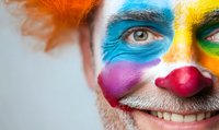 Close up portrait of smiling male clown with colorful face paint, red nose, and vibrant makeup showing partial face against white background for entertainment and carnival concepts.