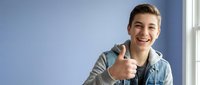 Young Caucasian man in denim jacket giving thumbs up gesture with confident smile in modern office or home interior for success and approval concepts.
