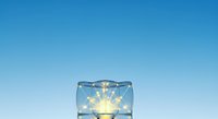 Light bulb glowing inside transparent glass cube against clear blue sky, symbolizing innovation, creativity, and bright ideas for business and technology concepts.