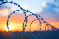 Razor wire silhouette against dramatic orange and blue sunset sky creates powerful metaphor for boundaries, security, and restriction in modern society.