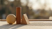 Wooden geometric shapes circle cylinder triangle arranged on natural wood surface with warm sunlight and bokeh background for design projects.