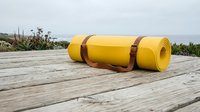 Yellow foam exercise mat rolled up with leather straps on wooden deck outdoors for fitness yoga pilates workout training equipment gear.