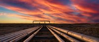Industrial pipeline infrastructure stretching across desert landscape under dramatic orange and purple sunset sky for energy and oil industry concepts.