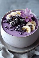 Purple smoothie bowl with frozen blackberries, banana slices, blueberries and edible flower garnish in ceramic bowl on gray background. Food styling.