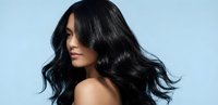 Young Asian woman with long flowing black hair in motion against light blue background showcasing healthy shiny hair for beauty and haircare concepts.