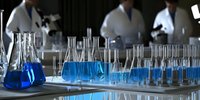 Laboratory glassware with bright blue liquid on white table, scientists working in background. Research facility with flasks and beakers for chemistry experiments.