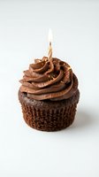 Chocolate cupcake with rich cocoa frosting and lit birthday candle on white background, suitable for bakery, celebration, and dessert marketing.