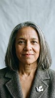 Confident mature Hispanic businesswoman with gray hair in professional suit smiling warmly at camera for corporate headshot and leadership content.