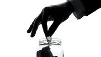 Silhouette of hand dropping coin into glass jar against white background, savings and investment concept for financial growth and money management.