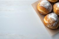 Fresh homemade donuts dusted with powdered sugar on kraft paper against white wooden background, corner composition with copy space for text.