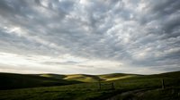 Dramatic rolling hills with lush green meadows under stormy cloudy sky, suitable for landscape and nature backgrounds.