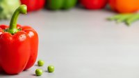 Fresh red bell pepper with green peas on white surface, colorful vegetables in soft focus background for healthy cooking and nutrition concepts.