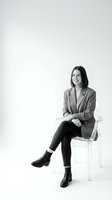 Professional Asian businesswoman in blazer sitting on transparent chair smiling confidently in black and white studio portrait for corporate use.