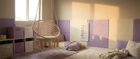 Modern teenage bedroom interior with hanging wicker chair, purple accent wall panels, cozy bedding and natural sunlight streaming through window.