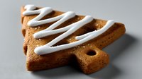 Christmas tree shaped gingerbread cookie with white icing drizzle on gray background, festive holiday baking treat.