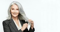 Mature woman with long gray hair wearing dark blazer, smiling at camera against white background. Corporate portrait for business, professional headshot, and executive branding use.